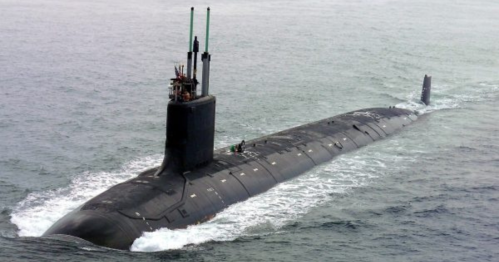 A submarine surfaces in the ocean, with crew members visible on top and waves splashing around it.