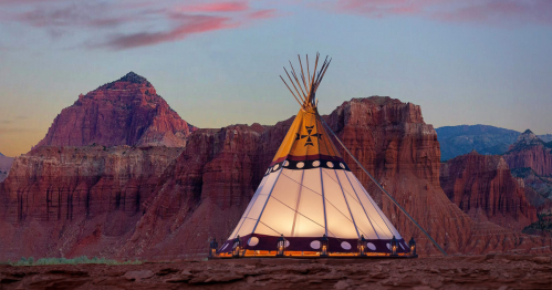 A colorful teepee stands against a backdrop of red rock formations and a twilight sky.