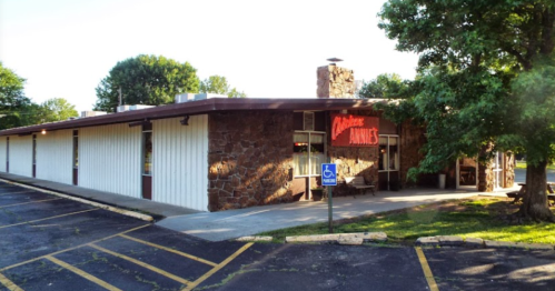 A stone and metal building with a sign reading "Annie's," surrounded by trees and a parking lot.