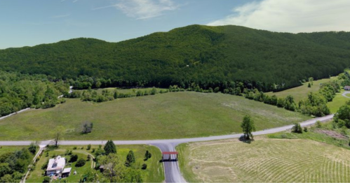 Aerial view of a green landscape with rolling hills, fields, and a road intersecting a grassy area.