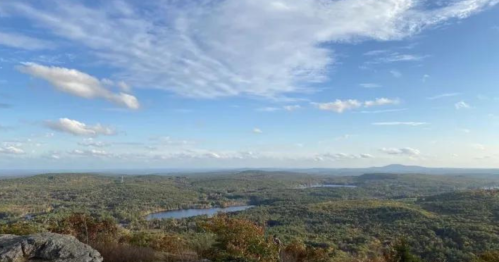 A scenic view of rolling hills, lakes, and a blue sky with scattered clouds.