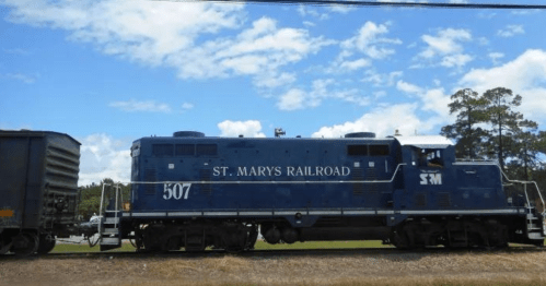 A blue St. Marys Railroad locomotive numbered 507 parked beside a freight car under a partly cloudy sky.