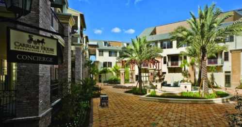 A sunny courtyard of a condominium complex featuring palm trees, a fountain, and a concierge sign.