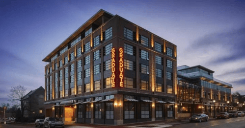 A modern hotel building with large windows, featuring a bright "Graduate" sign, set against a twilight sky.