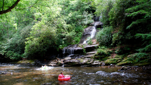 Two people float in tubes along a lazy river and next to a tall waterfall in North Carolina.