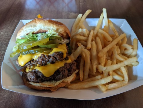A cheeseburger with lettuce, pickles, and fries on a tray.