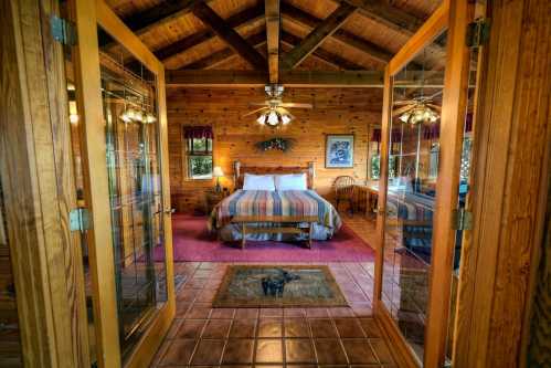 Cozy wooden cabin interior with a bed, ceiling fan, and large glass doors leading to a welcoming atmosphere.