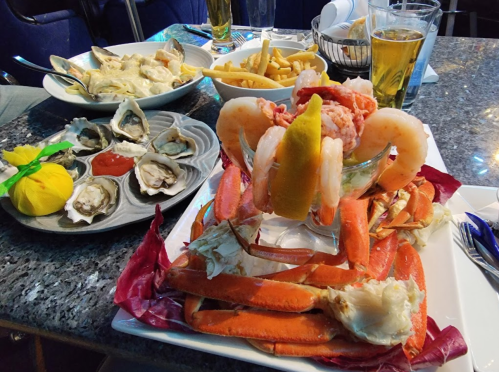 A seafood platter featuring shrimp, crab legs, oysters, fries, and drinks on a table.