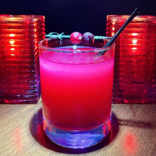 A vibrant pink cocktail garnished with cranberries, set against glowing red candle holders.
