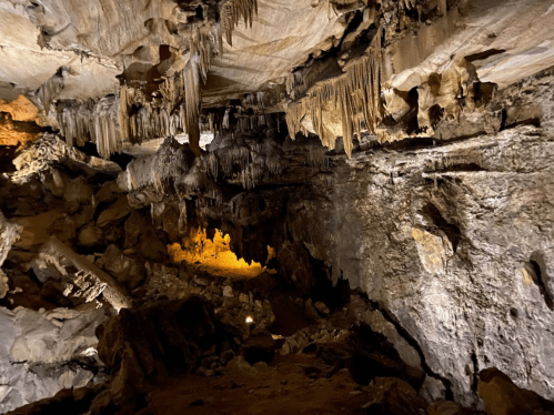 A dimly lit cave interior featuring stalactites and rock formations, with a warm glow from a light source.