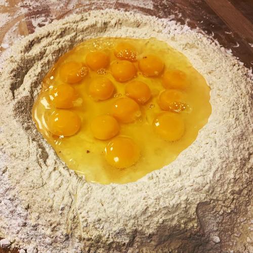A mound of flour with a well in the center filled with multiple raw egg yolks.