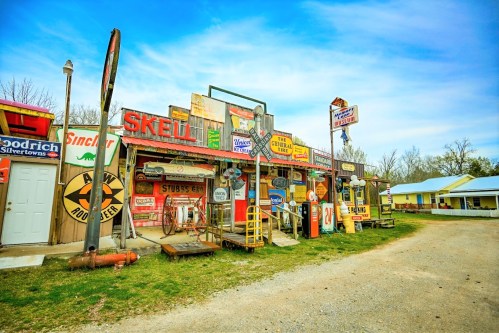 A vintage roadside shop adorned with colorful signs and memorabilia, set against a clear blue sky.