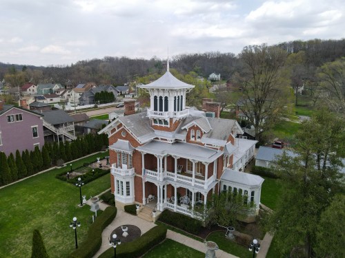 Aerial view of a large, ornate brick mansion with a white cupola, surrounded by green lawns and trees.