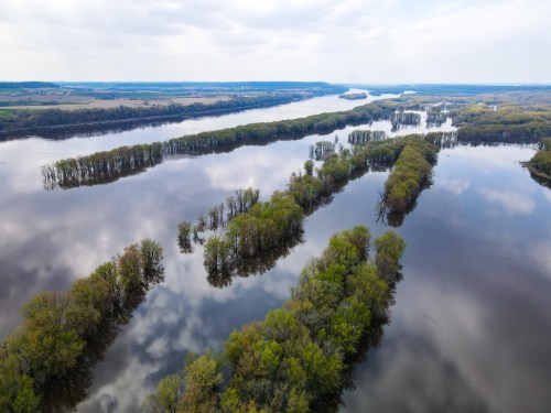 Aerial view of a river with lush green islands and reflections in the water, under a cloudy sky.