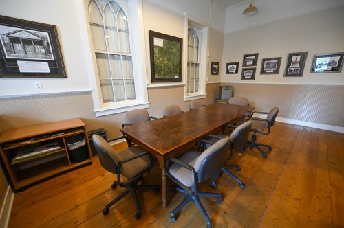 A spacious meeting room with a long wooden table and several chairs, featuring framed photos on the walls.