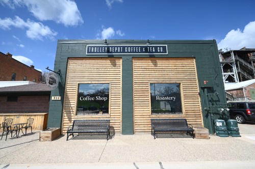 Exterior of Trolley Depot Coffee & Tea Co. featuring a coffee shop and roastery, with benches and a clear blue sky.