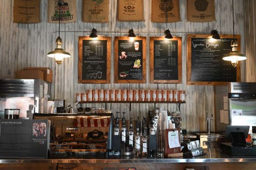 A coffee shop counter with menus, coffee equipment, and decorative bags on the wall.