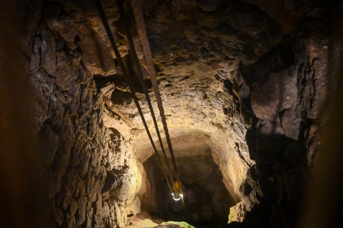A dimly lit cave with rocky walls and a light source illuminating the path below.