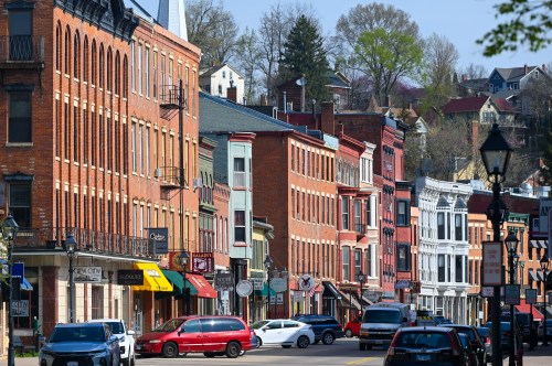 A charming street lined with historic brick buildings, shops, and parked cars under a clear blue sky.