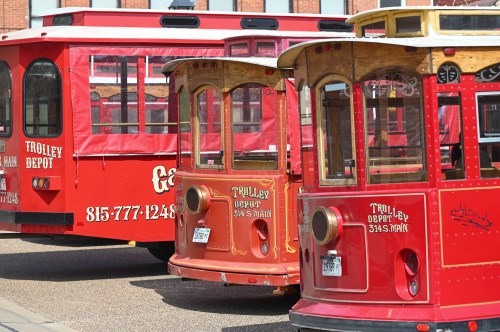 Two vintage red trolleys parked side by side, showcasing their wooden details and signage for a trolley depot.