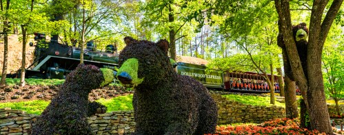 Topiary bears interact in a lush garden, with a vintage train passing by in the background.