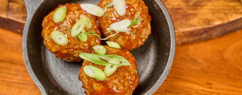 Three meatballs glazed with sauce and topped with sliced green onions, served in a small cast iron skillet.