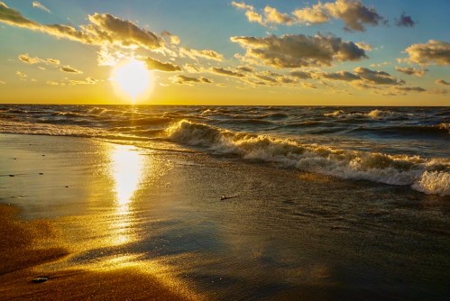 Sunset over a beach, with golden light reflecting on the water and waves gently rolling onto the shore.