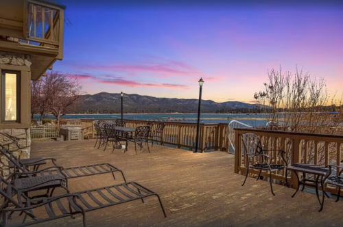 Scenic deck overlooking a lake at sunset, with chairs and mountains in the background.