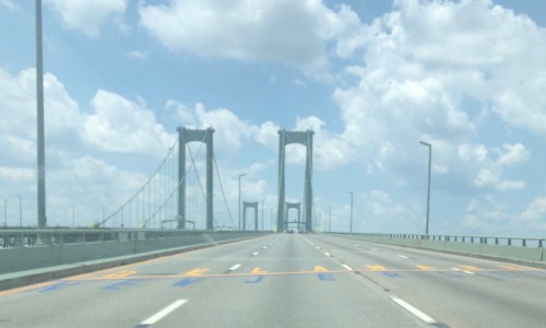 A view of a bridge with tall towers, connecting Delaware and New Jersey, under a partly cloudy sky.