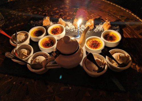 A dessert platter featuring crème brûlée, ice cream, and a candle, arranged on a dark wooden table.