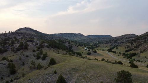 A scenic view of rolling hills and mountains under a cloudy sky, with a small structure in the distance.