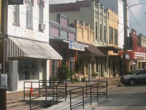 A row of colorful antique shops and storefronts along a quiet street, with a ramp and parked car in the foreground.