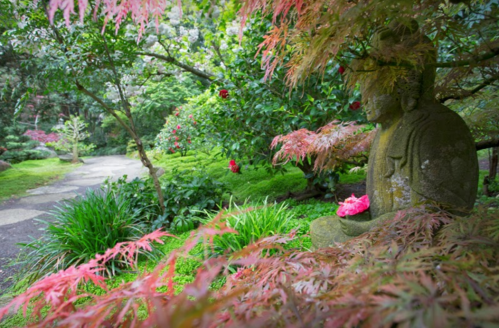 A serene garden scene featuring a stone statue surrounded by vibrant greenery and colorful foliage.
