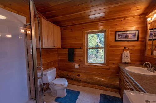 Cozy wooden bathroom featuring a shower, toilet, sink, and a window with natural light.