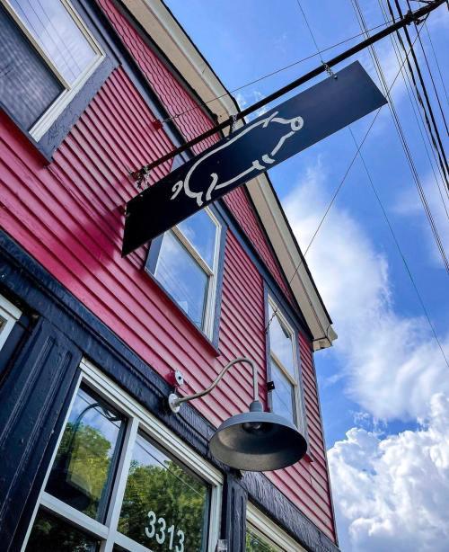 A red building with a black sign featuring a white abstract design, under a blue sky with fluffy clouds.