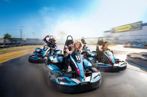Four people racing go-karts on a track, with vibrant colors and motion blur conveying speed and excitement.