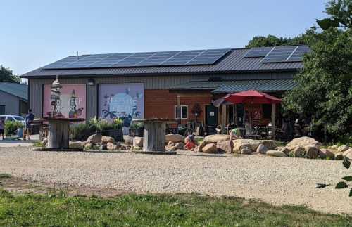 A rustic building with solar panels, outdoor seating, and a garden area, surrounded by gravel and rocks.