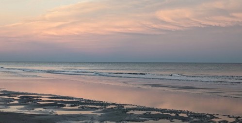 A serene beach at sunset, with gentle waves and soft pastel colors reflecting on the water.