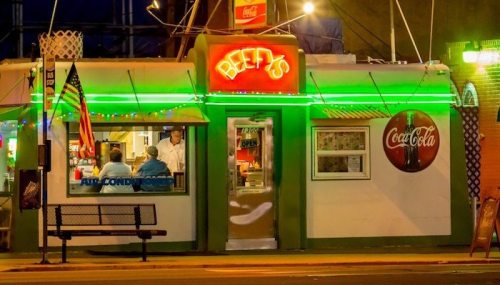 A brightly lit diner named "Beef's" with neon signs, featuring a Coca-Cola logo and outdoor seating.