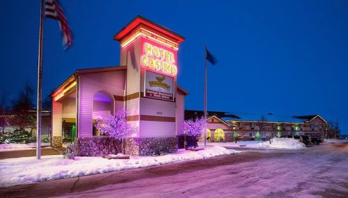 A brightly lit hotel and casino entrance at dusk, surrounded by snow and festive purple lights.