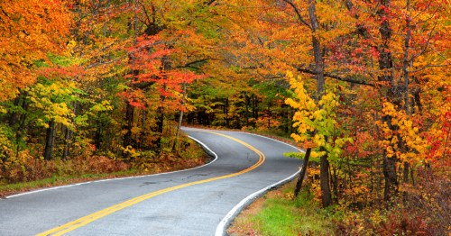 Vibrant fall foliage surrounds a two-lane highway in Vermont.