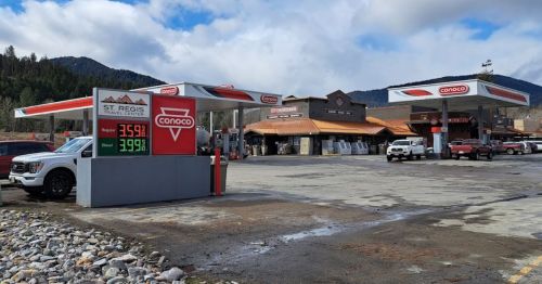 A Conoco gas station with a price sign showing fuel prices, surrounded by vehicles and mountains in the background.