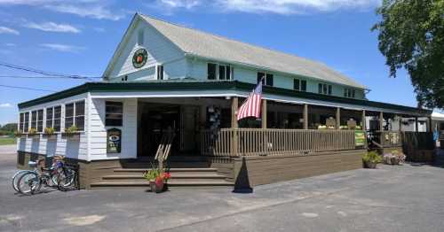 A white two-story building with a porch, American flag, and bicycles parked outside on a sunny day.