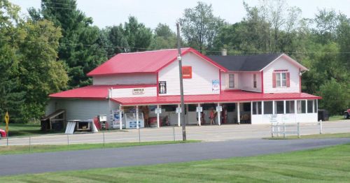 A two-story building with a red roof, featuring a storefront and surrounded by trees and grass.