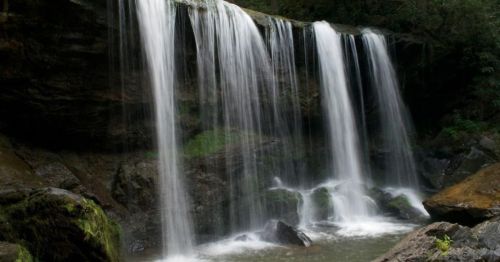 A serene waterfall cascading over rocks, surrounded by lush greenery and mist.