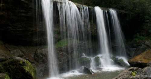 A serene waterfall cascading over rocks, surrounded by lush greenery and mist.