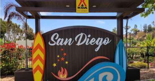 Sign for San Diego KOA Resort featuring colorful surfboards and vibrant landscaping.