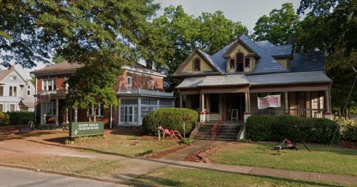 Two historic houses side by side, one with a porch and a "For Sale" sign, surrounded by green lawns and trees.