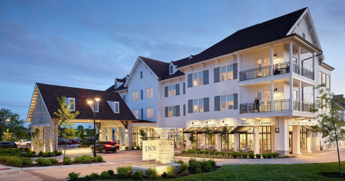 A modern inn with a white exterior, balconies, and landscaped surroundings, illuminated at dusk.