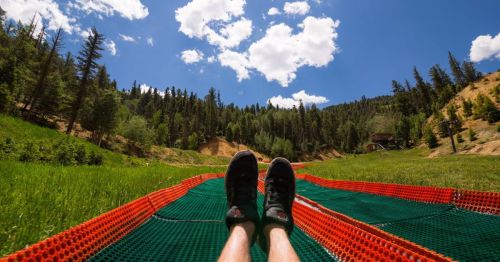 A person's feet on a colorful mat, with a lush green landscape and blue sky filled with clouds in the background.